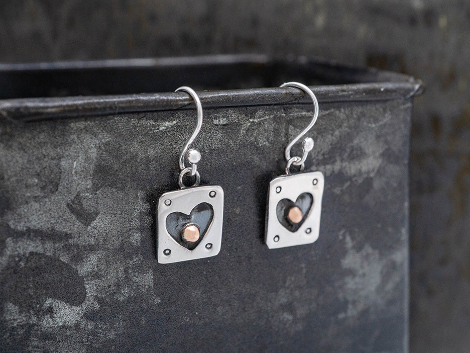 Silver earrings with heart designs on a dark textured surface