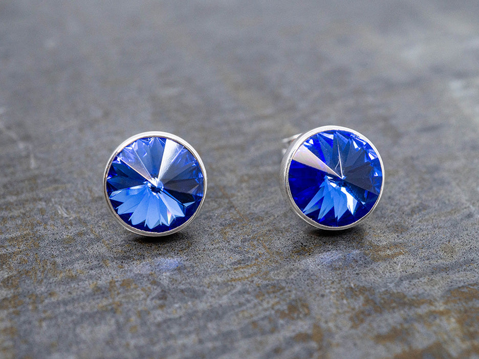 Pair of blue crystal stud earrings on a textured gray background