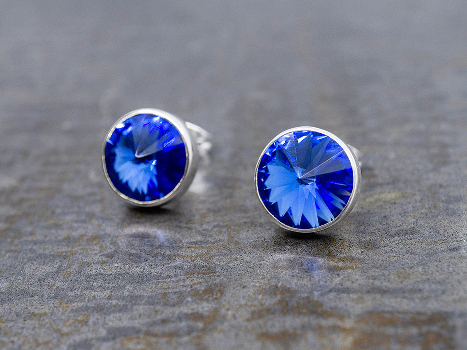 Pair of silver earrings with blue crystals on a stone surface