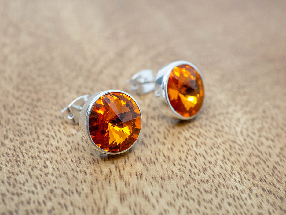 Pair of silver earrings with amber-orange crystals on a wooden surface