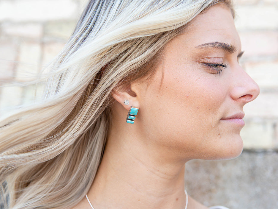 A model wearing a turquoise mosaic earring, featuring three turquoise stones. 