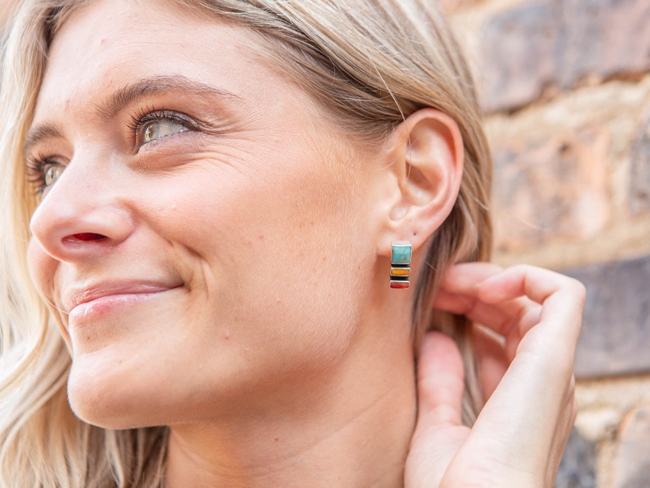 A model wearing a sterling silver earring featuring three stones, one turquoise, one yellow and one coral.