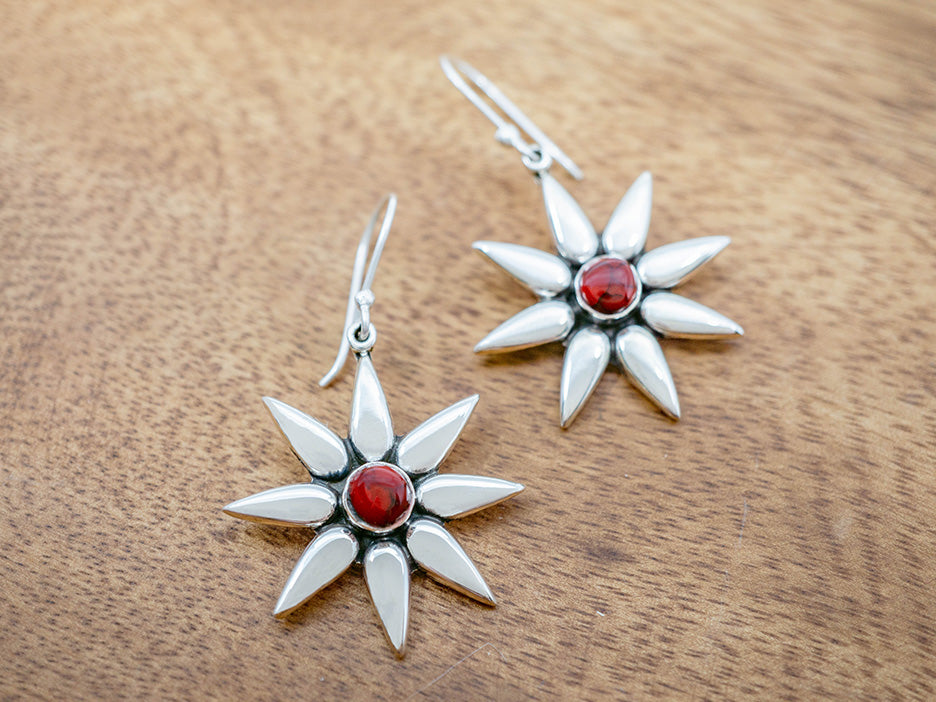 A pair of sterling silver starburst hook earrings with oxidized details and a red jasper stone in the center.