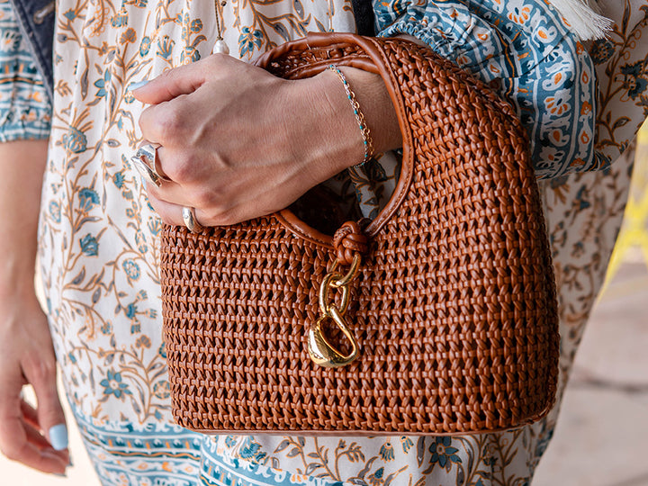 Person holding a brown woven handbag with a floral patterned garment.