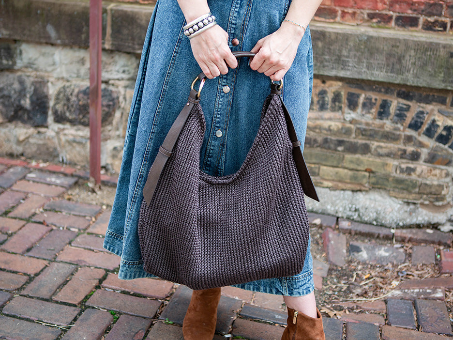 woman holding a large, dark brown mesh tote with both hands.