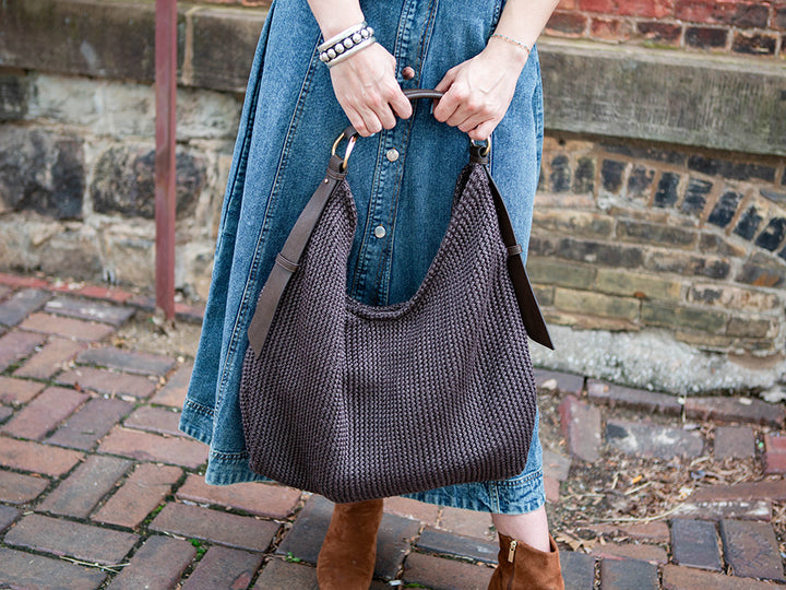 woman holding a large, dark brown mesh tote with both hands.