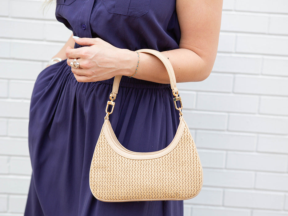 Person holding a beige handbag against a white brick wall