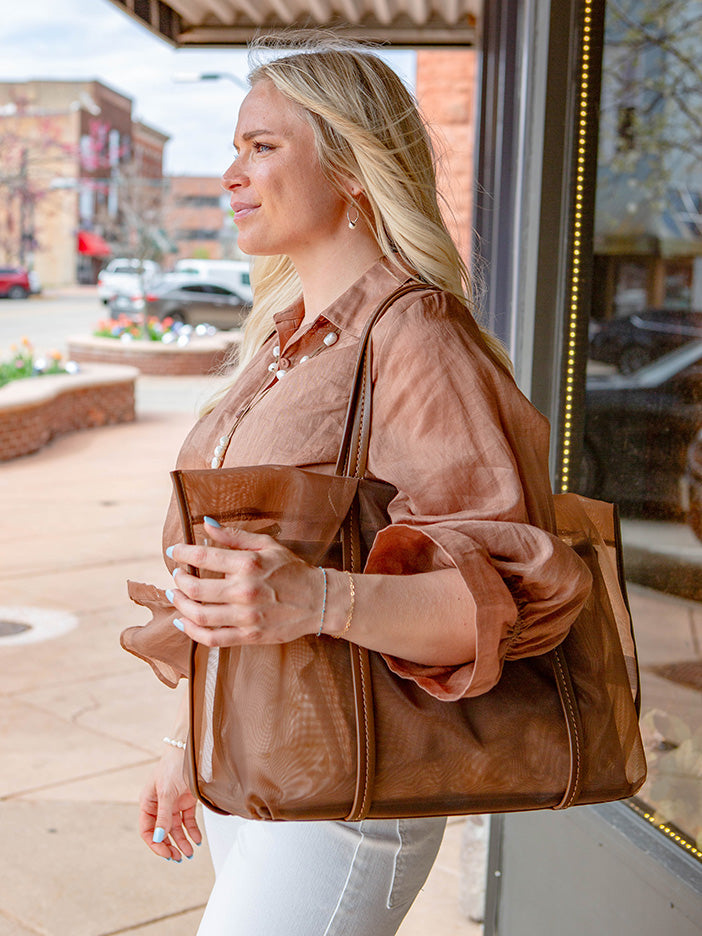 Woman holding a large brown handbag on a city sidewalk