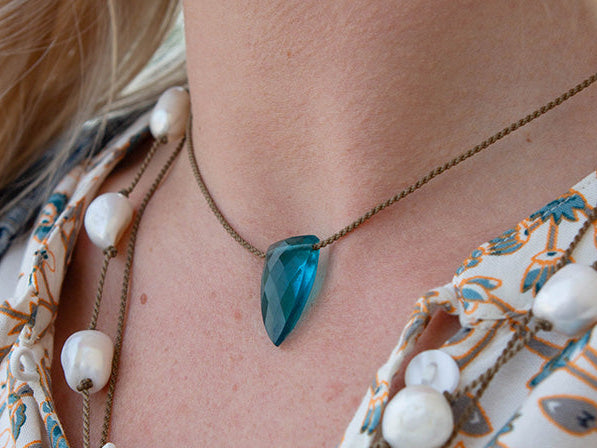 Close-up of a necklace with a blue pendant and pearls on a patterned garment.