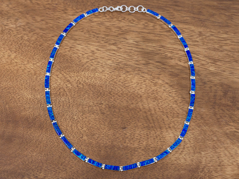 A sterling silver necklace made of hinged rectangular links. Each silver link has dark blue opal set in it. 