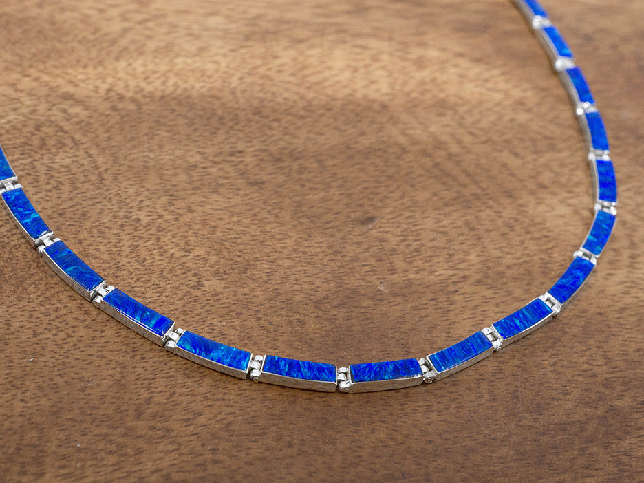 A sterling silver necklace made of hinged rectangular links. Each silver link has dark blue opal set in it. 