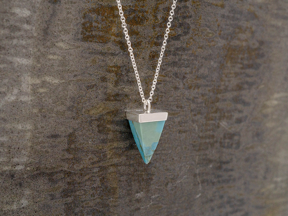 A small, upside-down pyramid of turquoise stone hanging on a silver chain.