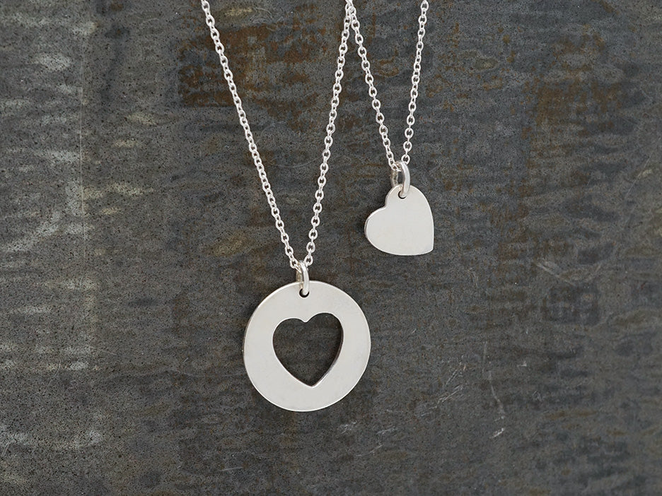 Two sterling silver necklaces, one a silver heart and one a circle with a heart-shaped cutout.