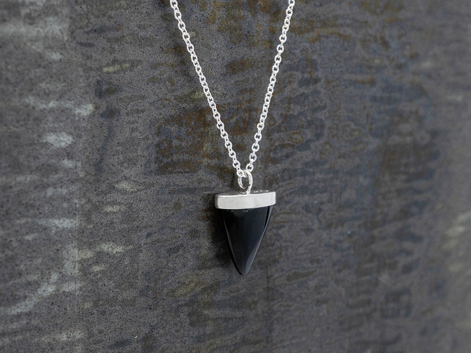 Black triangle-shaped pendant on a silver chain against a textured gray background