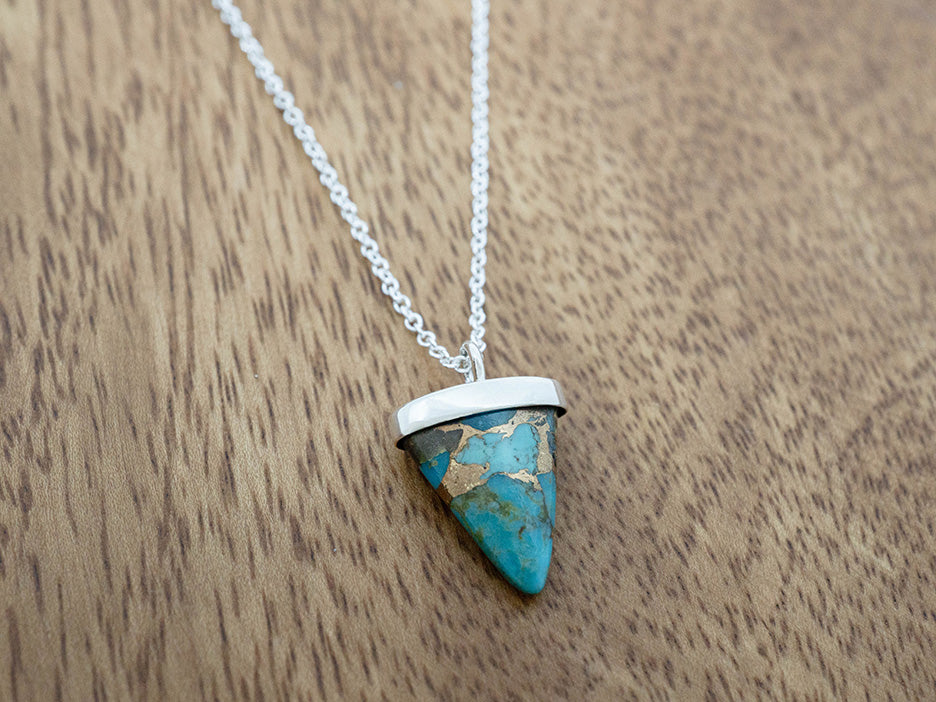 Turquoise triangle pendant necklace on a wooden surface