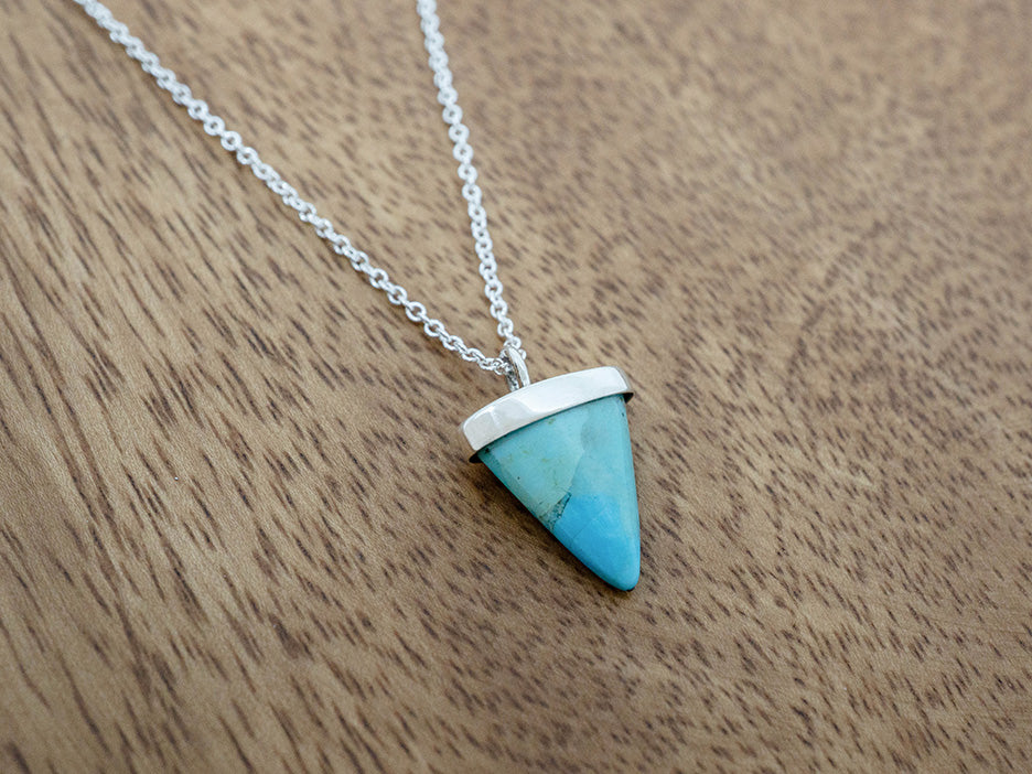 Turquoise triangle pendant necklace on a wooden surface