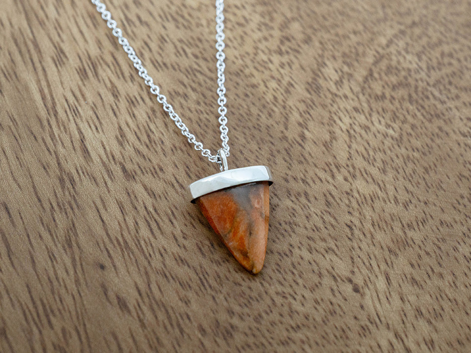 Silver necklace with a triangular sponge coral pendant on a wooden surface