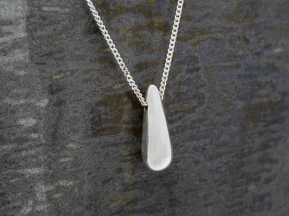 Silver necklace with a teardrop-shaped pendant on a textured gray background