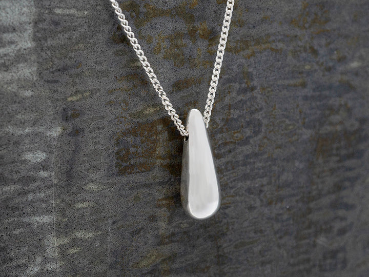 Silver necklace with a teardrop-shaped pendant on a textured gray background