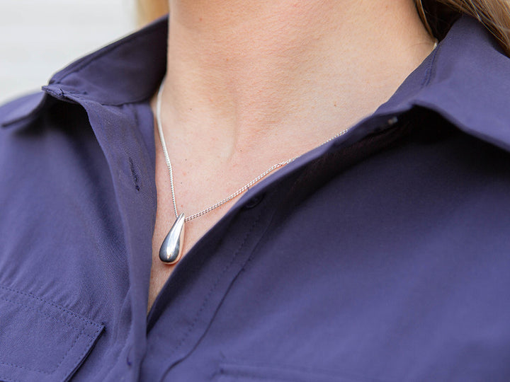 Person wearing a silver necklace with a teardrop pendant on a purple shirt.