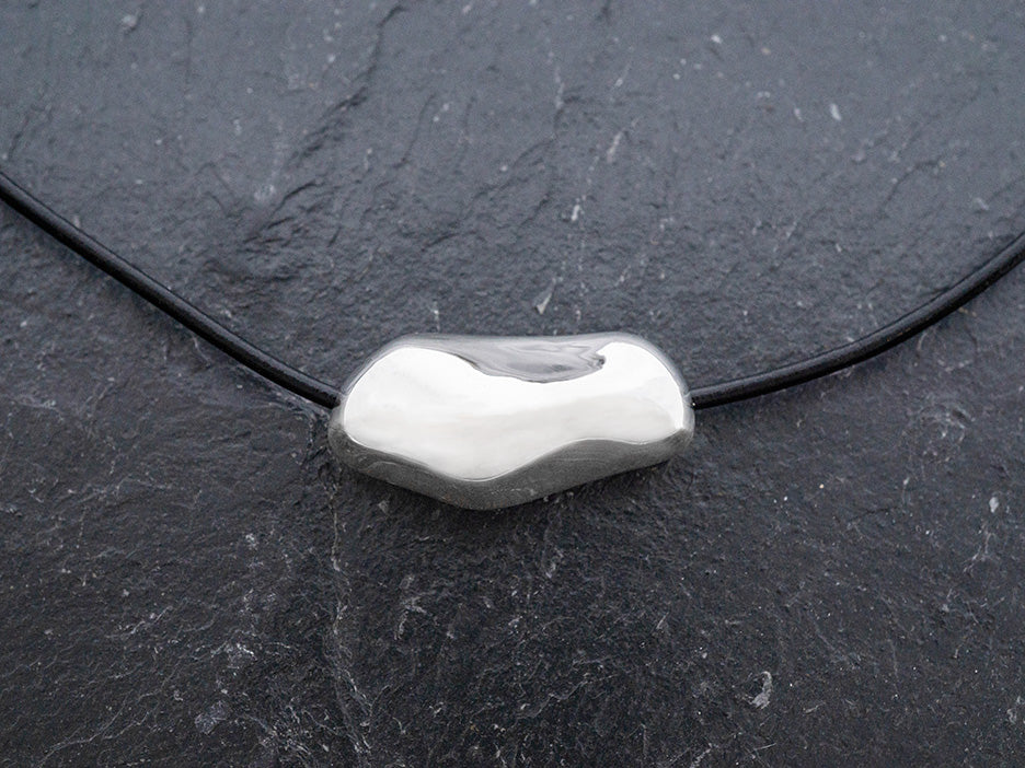 Silver pendant on a black cord against a dark background