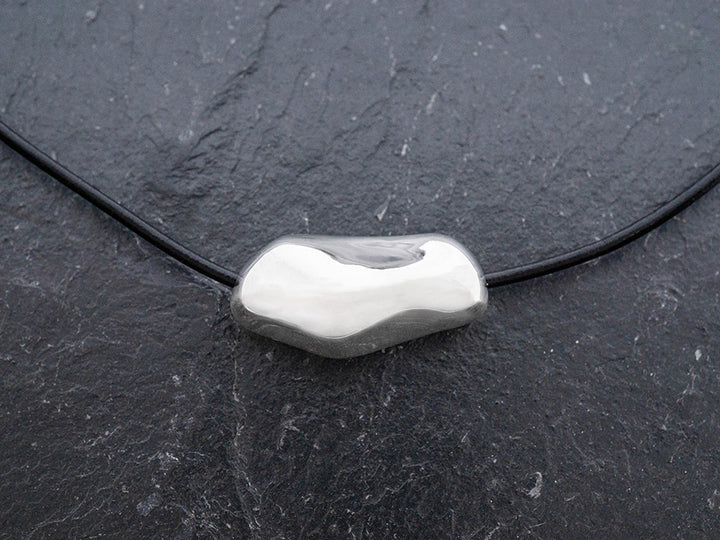 Silver pendant on a black cord against a dark background
