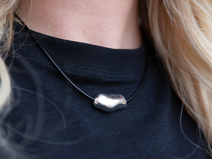 Close-up of a person wearing a black top with a silver pendant necklace.