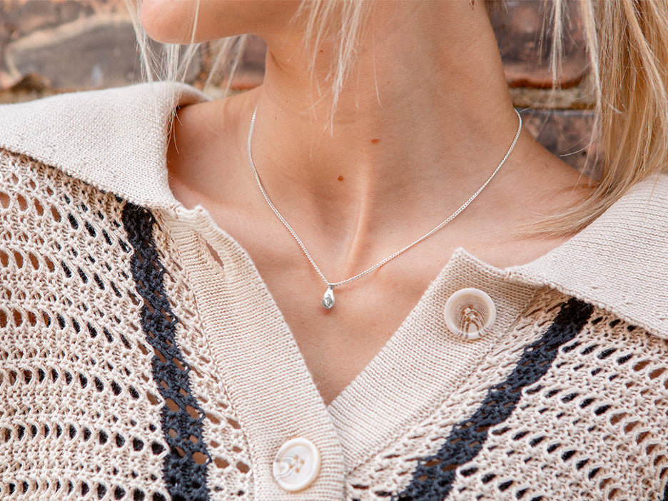 A model wearing a dainty sterling silver necklace with a teardrop in the center.