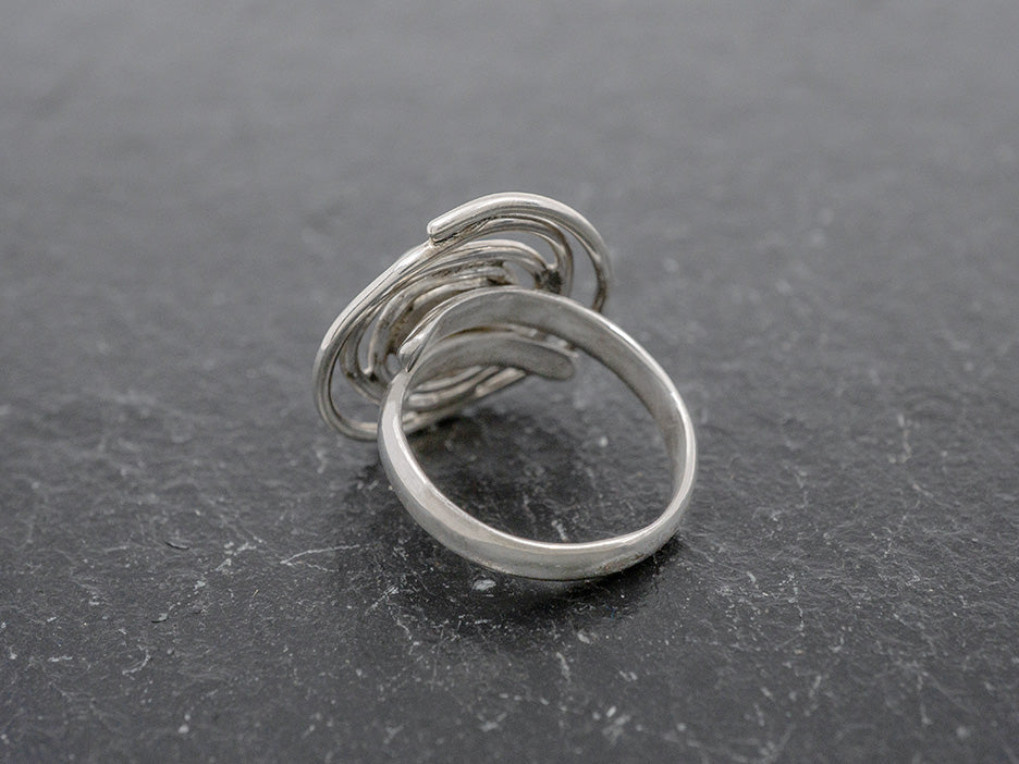 An adjustable ring featuring a cultured pearl at the center of a silver swirl.