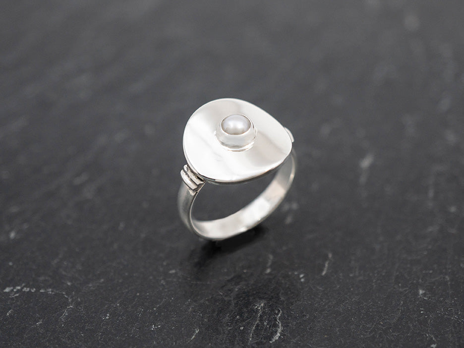 A sterling silver ring topped with a curved disc with a pearl in the center