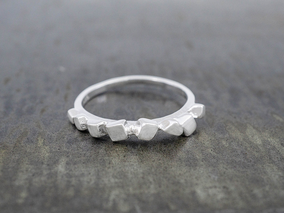 A close up on a single stackable ring that features a row of roughly cut silver squares at the top of the band.