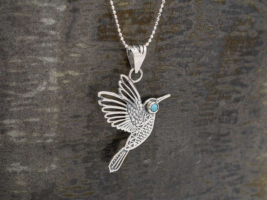 Silver hummingbird pendant with a turquoise stone eye on a dark textured background