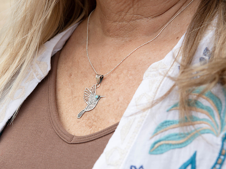 Close-up of a necklace with a bird pendant worn by a person.