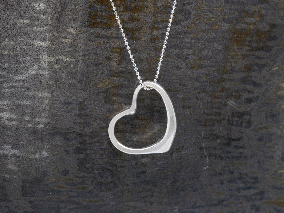 Silver heart-shaped pendant on a chain against a dark background