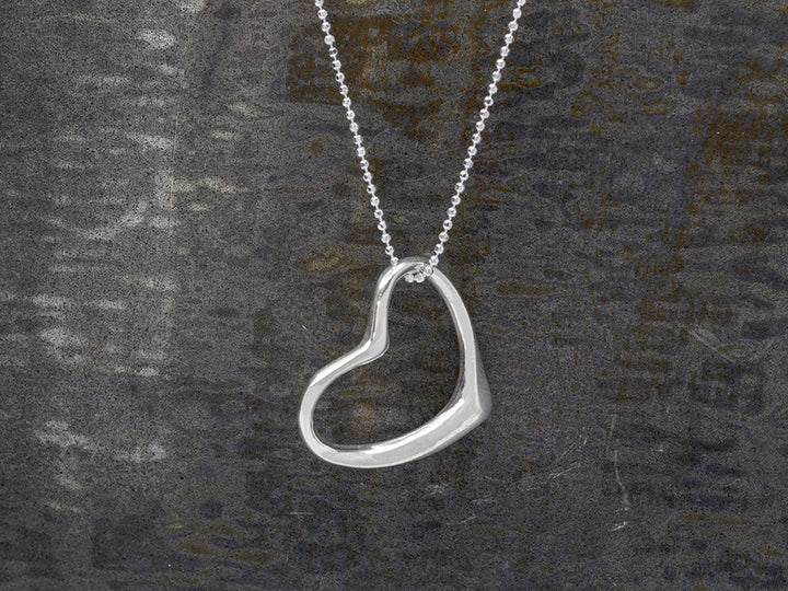 Silver heart-shaped pendant on a chain against a dark background