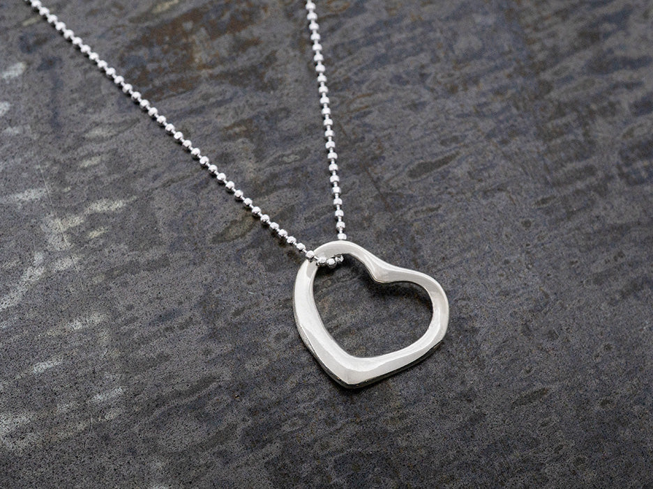 Silver heart-shaped pendant on a chain against a gray background