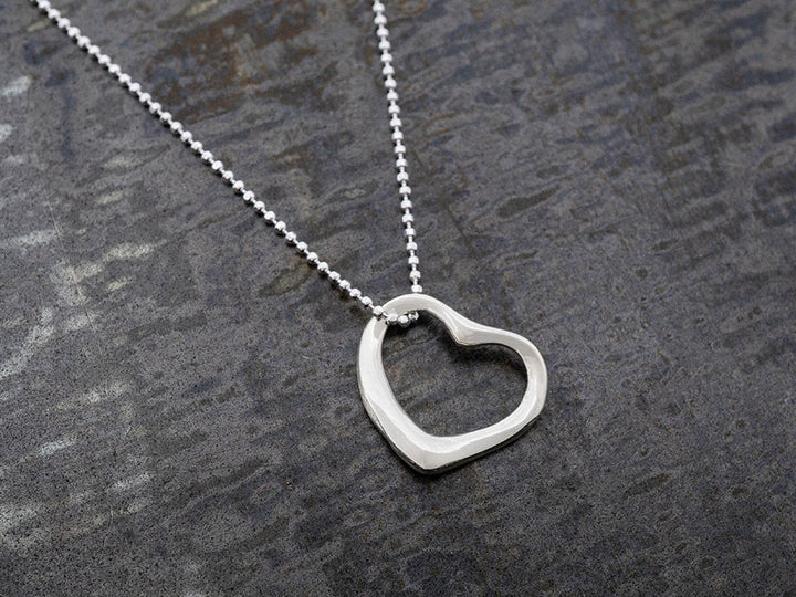 Silver heart-shaped pendant on a chain against a gray background