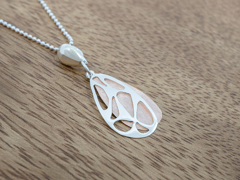 Silver & copper pendant necklace on a wooden surface. 