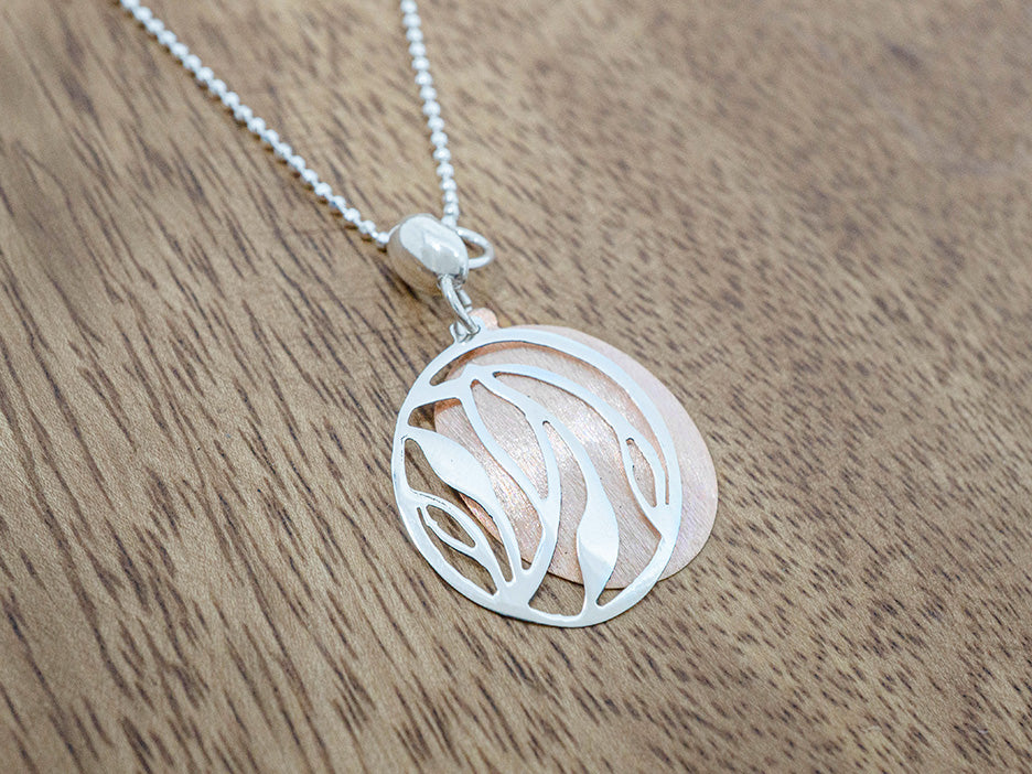 Silver and copper necklace with a circular pendant on a wooden surface
