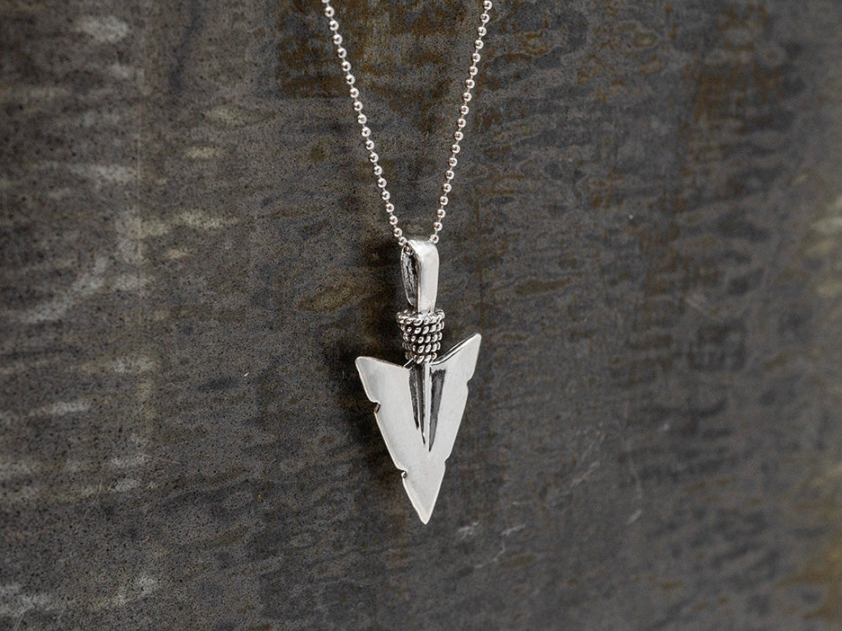 Silver arrowhead pendant necklace on a dark textured background