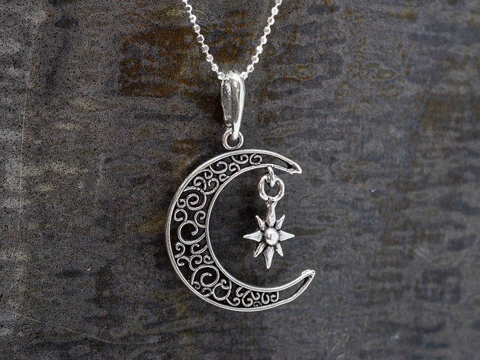 A sterling silver crescent moon pendant with intricate filigree work and a silvers star dangling inside the arc.