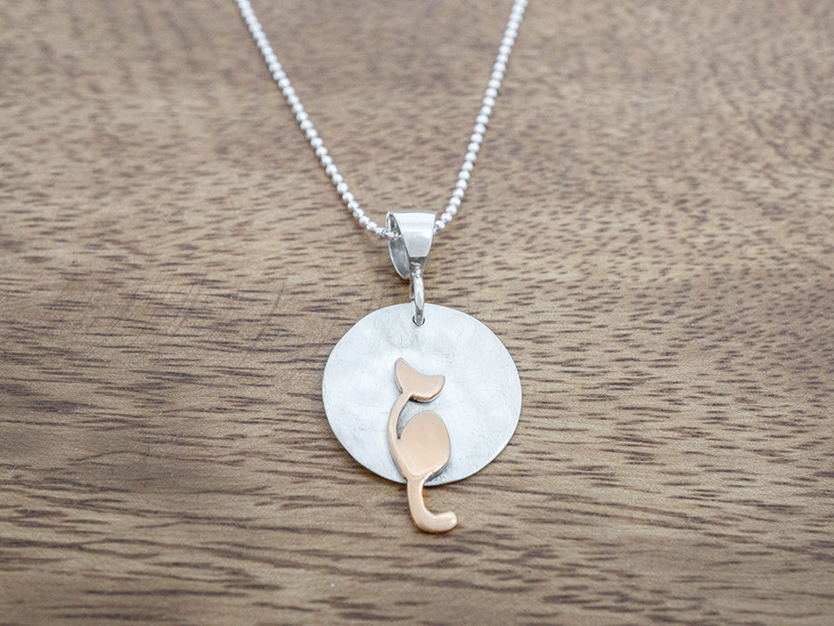 Necklace with a round pendant featuring a cat silhouette on a wooden surface