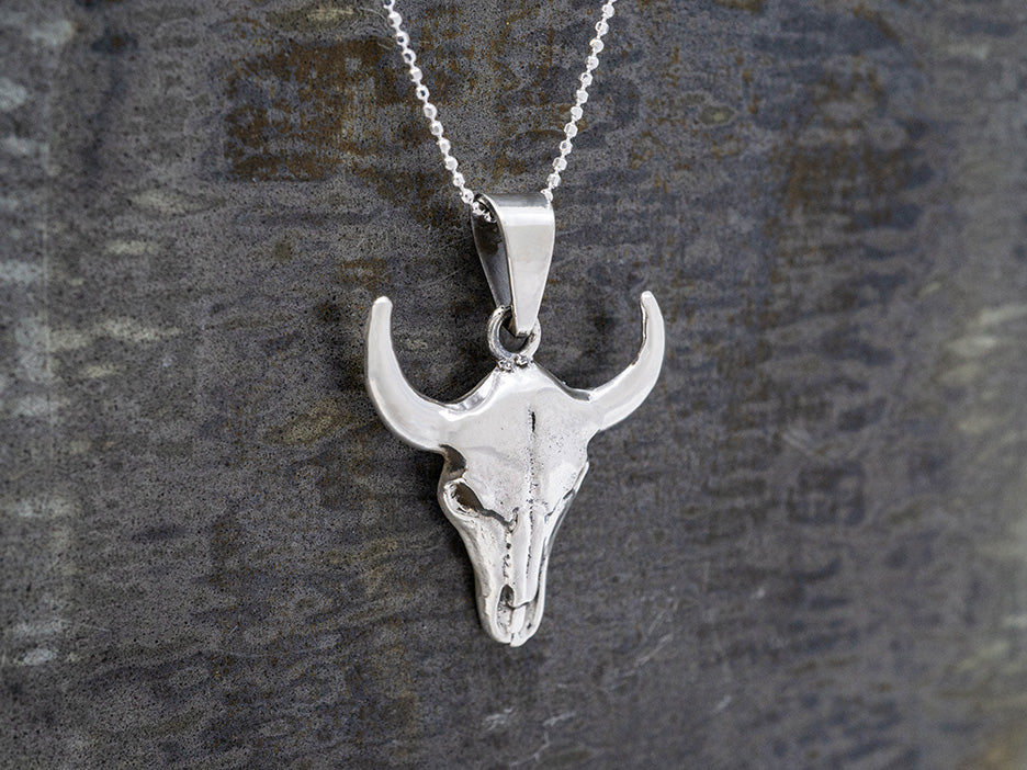 Silver bull steer head pendant on a chain against a textured gray background