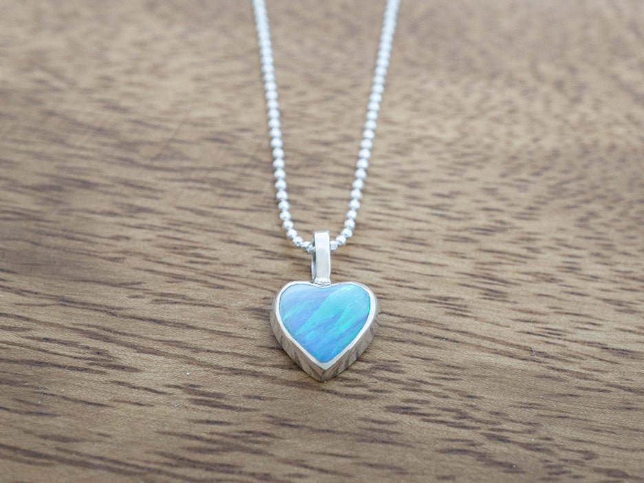 Heart-shaped blue opal pendant on a chain against a wooden background