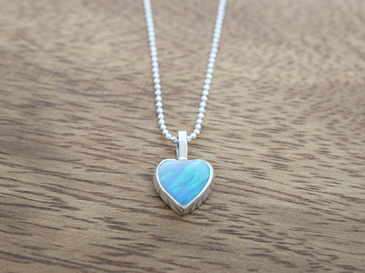 Heart-shaped blue opal pendant on a chain against a wooden background