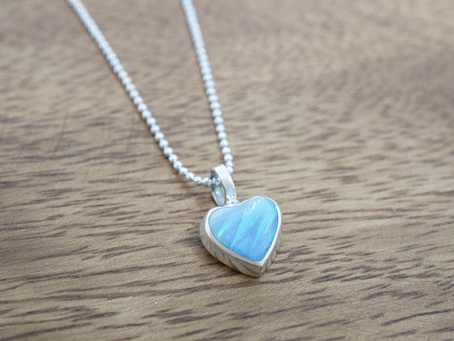 Heart-shaped blue opal pendant on a chain against a wooden background