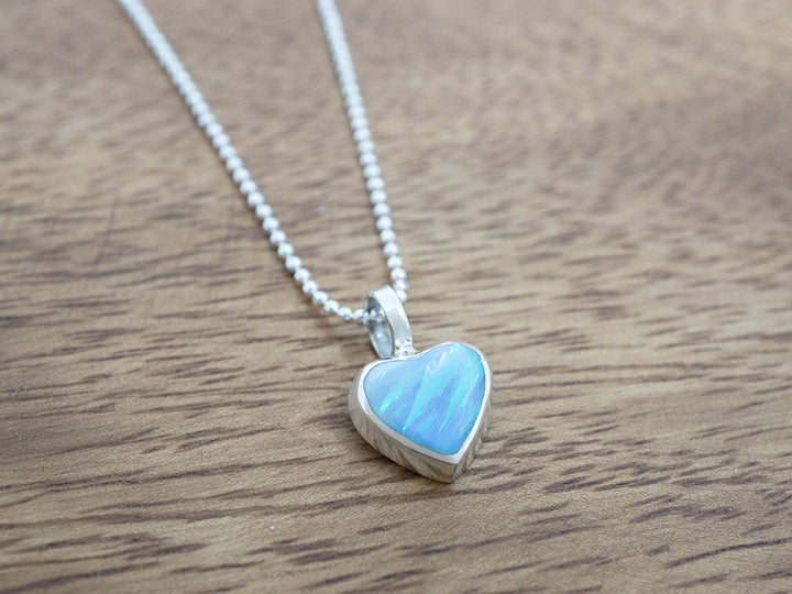 Heart-shaped blue opal pendant on a chain against a wooden background