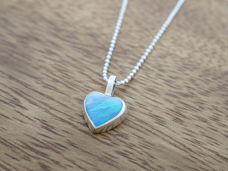 Heart-shaped blue opal pendant on a chain against a wooden background