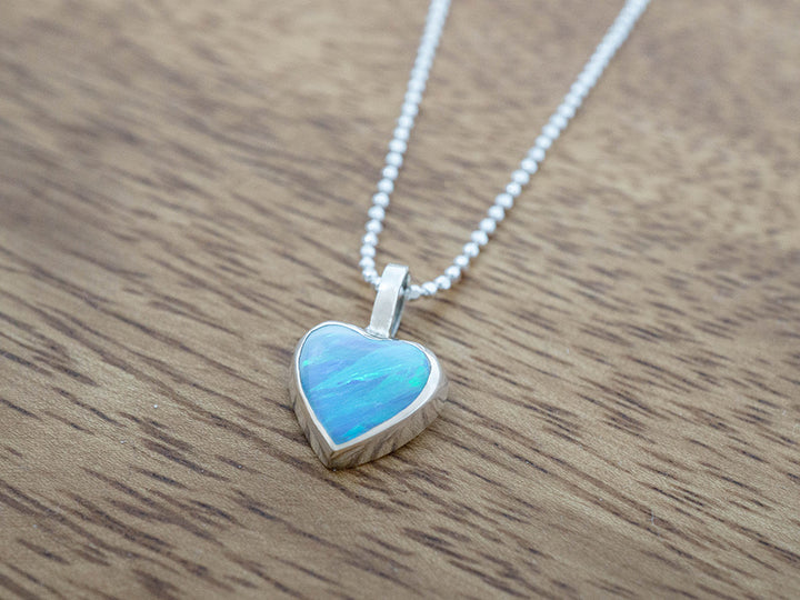 Heart-shaped blue opal pendant on a chain against a wooden background