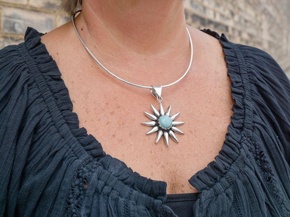 A model wearing a flexible sterling silver choker supporting a turquoise sunburst pendant.